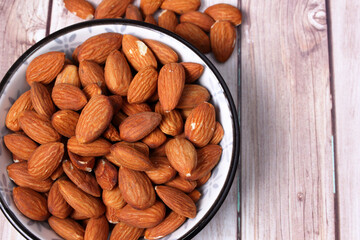 Mandorle californiane senza guscio disposte in una ciotola su sfondo di legno. Spazio per testo. Messa a fuoco selettiva.
