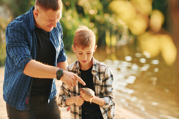 Holding the catch. Father and son on fishing together outdoors at summertime