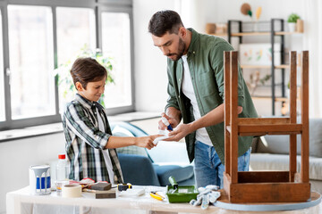 family, medicine and health concept - father healing son's injured finger with antiseptic at home