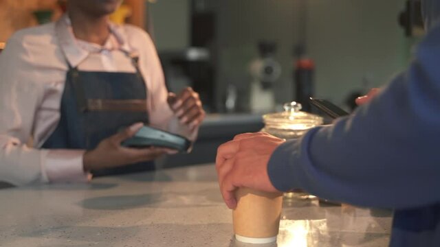 Takeaway black waitress and guest in shop. Spbas African-American woman gives drink and accepts payment with bank terminal from client in cafe closeup