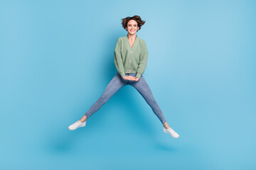 Fototapeta na wymiar Full length photo of charming funky young girl dressed green cardigan jumping high isolated blue color background