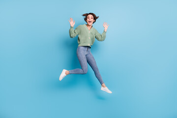 Fototapeta na wymiar Full length photo of impressed funny young lady wear green cardigan jumping high isolated blue color background