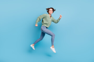 Fototapeta na wymiar Full length photo of sweet charming young girl dressed green cardigan jumping high running fast isolated blue color background