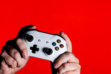 A photo of men hands holding a white gamepad on a bright red background with a place for the...