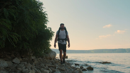 The attractive man with backpack walking along the shore