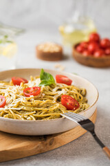 Spaghetti pasta with pesto sauce and cherry tomatoes in a plate close-up.