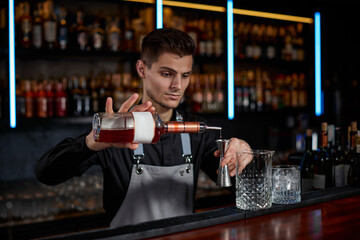 Bartender in apron adds ingredient to glass