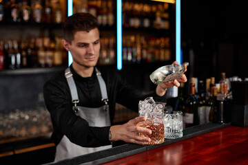 Barman puts the ice cubes into a glass with alcoholic drink