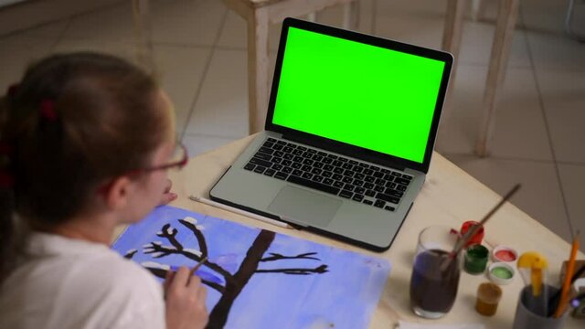 Online creativity development with internet resources. Spbas Child with plait draws winter tree during video lesson via laptop with chromakey screen at home