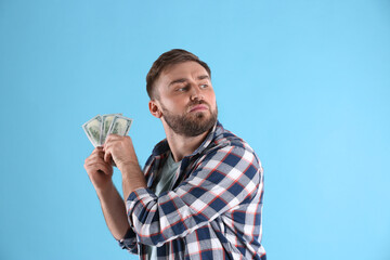 Greedy young man hiding money on light blue background - obrazy, fototapety, plakaty