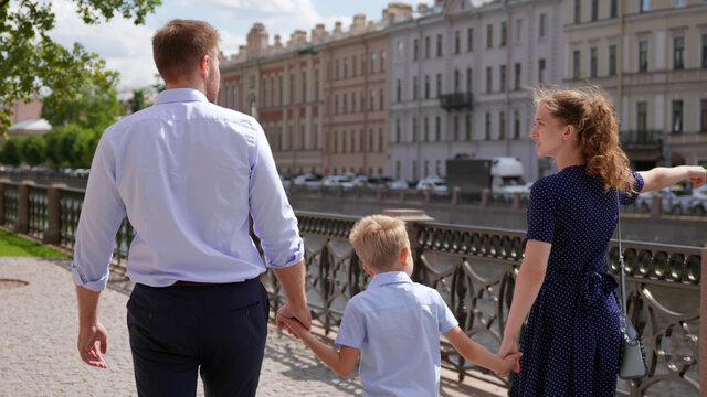Back view of mother, father and son hold hands walking in city center