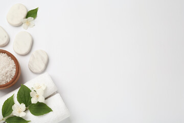 Spa stones, beautiful jasmine flowers, sea salt and towels on white background, flat lay. Space for...
