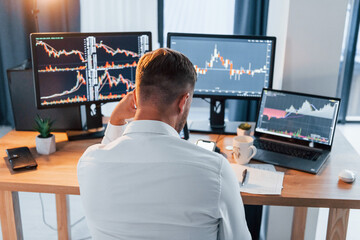 Hard working. Young businessman in formal clothes is in office with multiple screens