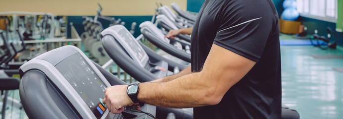 Unrecognizable man setting control panel of treadmill for training in the gym