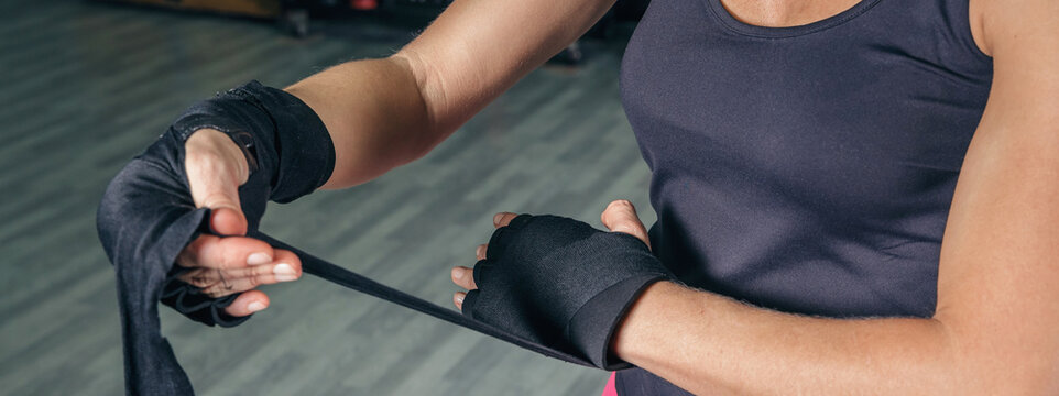Closeup of unrecognizable sportswoman wrapping her hands with protective bandages before boxing training in the gym - Powered by Adobe