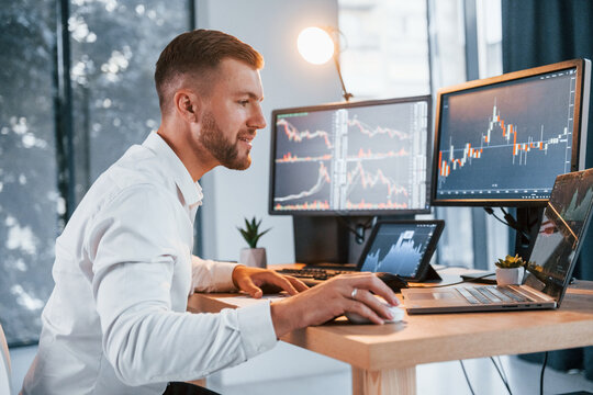 Stock market. Young businessman in formal clothes is in office with multiple screens