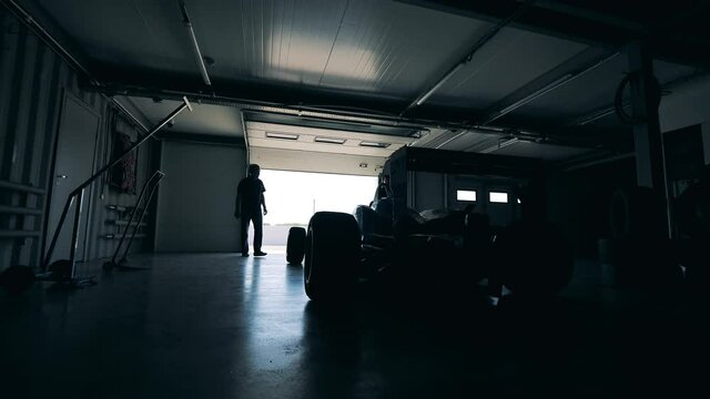 Two men are opening a garage with a racing car in it