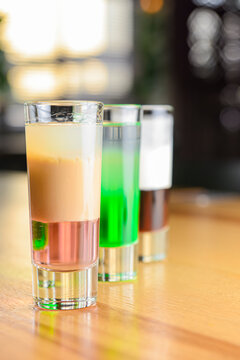 Three kinds of alcoholic drinks in shot glasses obn a wooden table over blurred background.