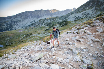 Fototapeta na wymiar man and white dog trekking in mountains over glacier lake - slow travel
