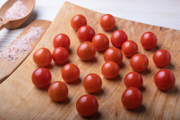 Close-up of appetizing small red cherry tomatoes on a natural wooden surface, next to a wooden spoon and a wooden spatula with coarse pink salt.