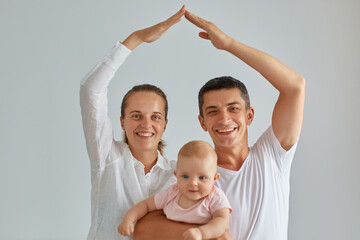Indoor shot of happy positive family posing isolated light background, looking at camera, holding...
