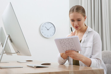 Young woman solving sudoku puzzle at workplace in office