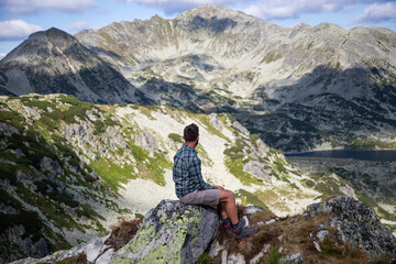 Naklejka na ściany i meble handsome man sitting on mountain top in amazing summer landscape