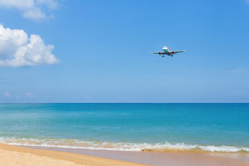 Fototapeta na wymiar Landscape view contained with blue sky and sea, golden sand while air plane landing on runway near the coast.