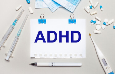 Fototapeta premium On a light gray background, blue medical masks, syringes, an electronic thermometer, pills, a pen and a notebook with the inscription ADHD. Medical concept
