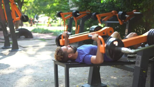 Open air gym. Street training on the municipal sports simulators. Athletic man doing bench press using outdoor training machine.