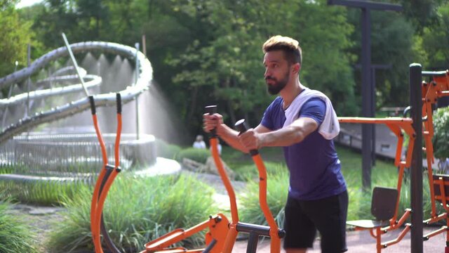 Open air gym. Street training on the municipal sports simulators. Athletic man is jogging on outdoor orbitrack machine. 
