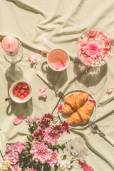 Sunny aesthetic picnic breakfast with flowers floating in crystal vases, croissants with tea from rose petals , bouquet of flowers and candles on blanket. Top view. Outdoor - 453794663