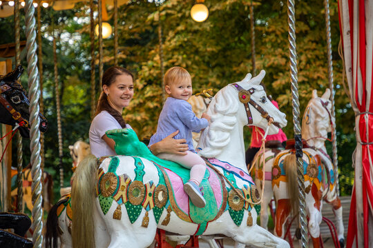 Cute baby girl with mother on the horse of old retro carousel, Prague, Czech republic 