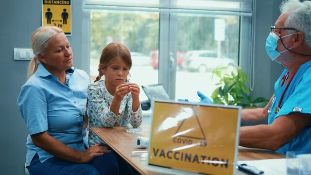 A little girl with her grandmother on vaccination at the hospital. The child holds a glass ampoule with the medicine against covid-19. Family is informed and compiles data in the vaccination center