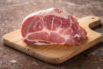 fresh raw pork neck meat fillet in wooden cutting board on rusty texture background, ingredient for chop steak