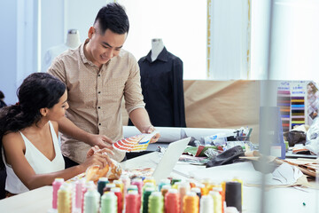 Cheerful young dressmakers discussing palette of samples when choosing fabric for new collection