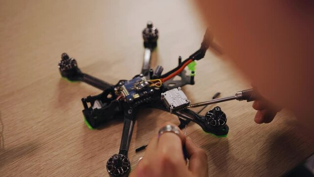The guy is soldering an electric chip with a hot soldering iron. He collects the drone on the table