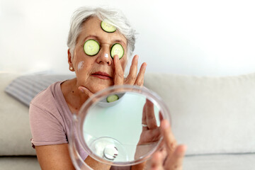 A senior woman with cucumber on front of his eyes, indoors. Beautiful old woman doing spa treatments at home. Natural homemade facial masks. Caucasian woman using natural secrets to do a skin care.