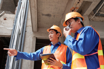 Contractors with tablet computer using walkie-talkie to control work of builders at construction site