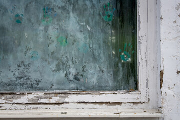 Schmutzige Scheibe in einem verwitterten Fensterrahmen mit bunten handabdrücken aus Fingerfarbe, verlassener Kindergarten, Schule ect