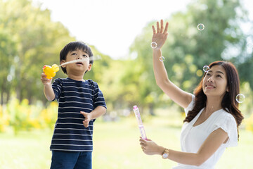 Happy Asian family spending time together outdoor on holiday. Asian mother and little boy playing with soap bubbles outdoor in the park. Smiling Toddler little boy having fun, enjoy with soap bubbles