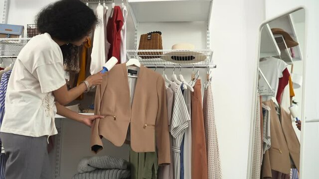 Wardrobe taking care of clothes supplies. Spbd African-American woman removes dirt from elegant jacket with lint roller in modern closet room of penthouse