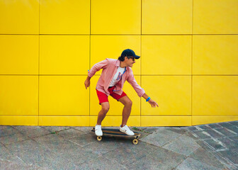 middle-aged man skateboarding on a yellow background. he is smiling.