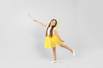 Cute little girl in fairy costume with yellow wings and magic wand on light background