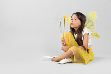 Cute little girl in fairy costume with yellow wings and magic wand on light background. Space for...