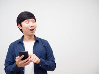 Asian young man holding and press mobile phone in his hand feeling excited and lookign at copy space white isolated