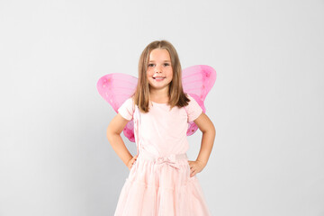 Cute little girl in fairy costume with pink wings on light background