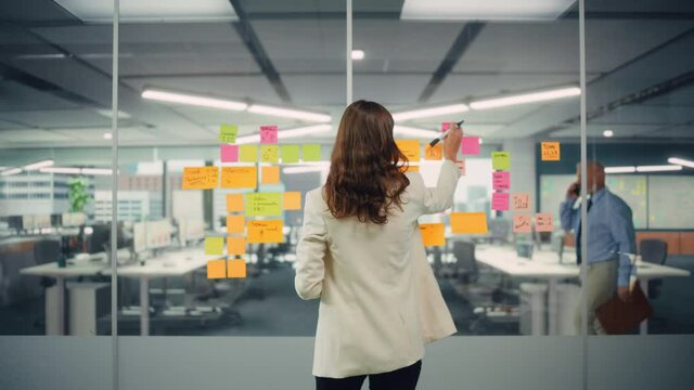 Young Confident Businesswoman Creating Project Plan on Office Wall with Paper Notes. Stylish Beautiful Manager Working on Business, Financial and Marketing Projects. Specialist in Diverse Team.