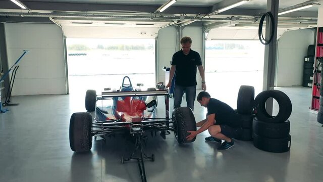 Two men are fixing wheels of a racing car