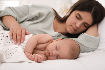Young mother resting near her sleeping baby on bed at home